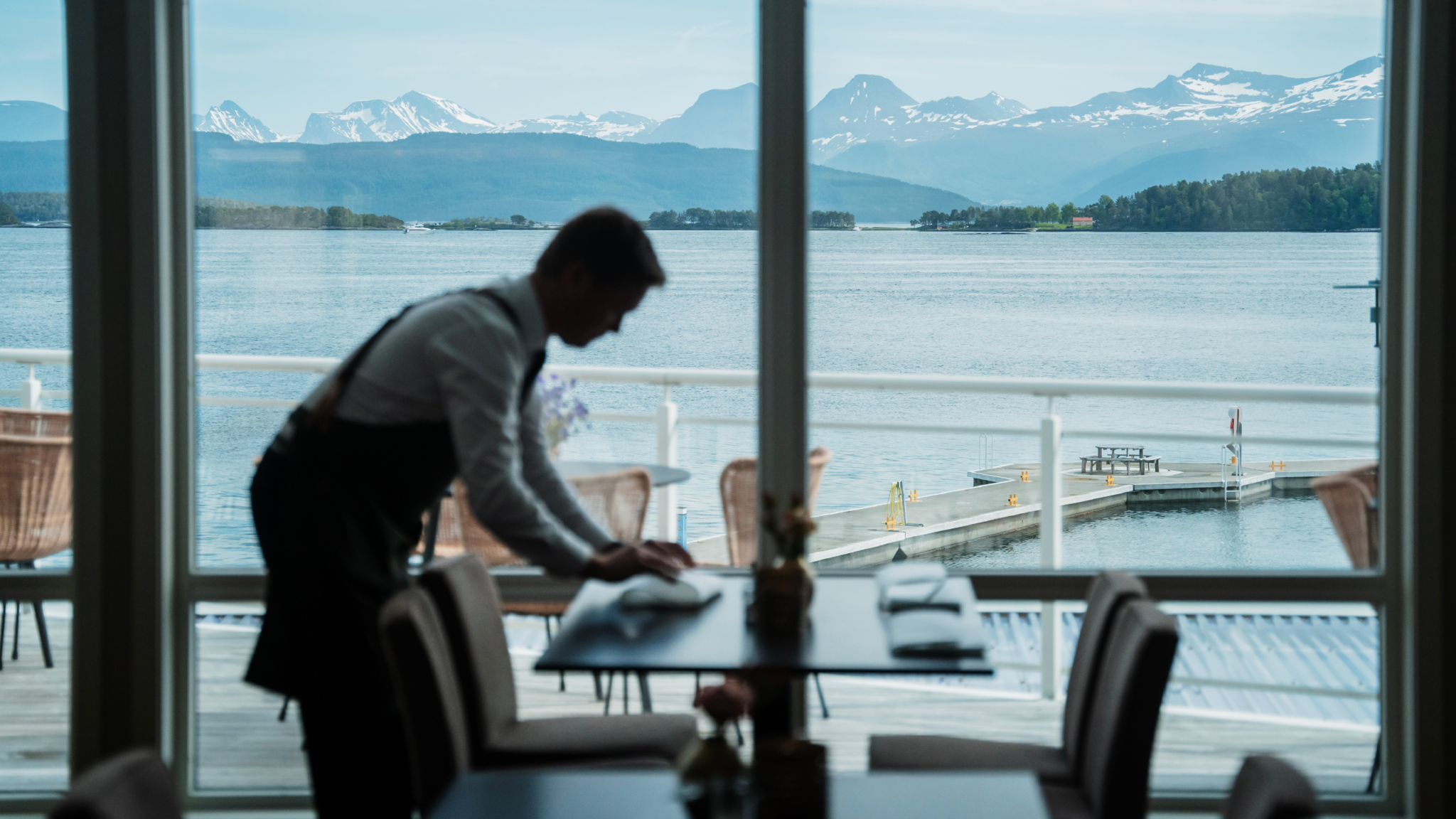 Foto fra Molde fjordhotell. Motivet er fra restauranten med fjorden og fjellene skarp i bakgrunnen, mens det står en servitør og dekker bord i forkant.