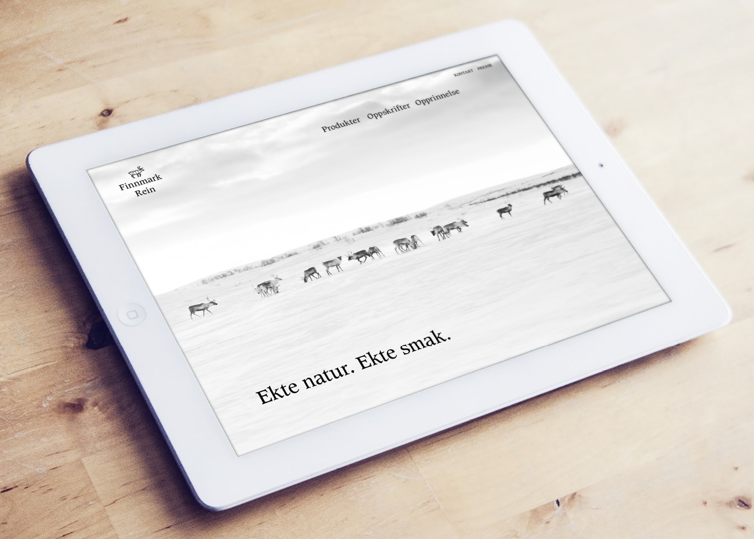 Foto av en hvit iPad som ligger på et trebord. På skjermen vises nettsiden til Finnmark Rein.